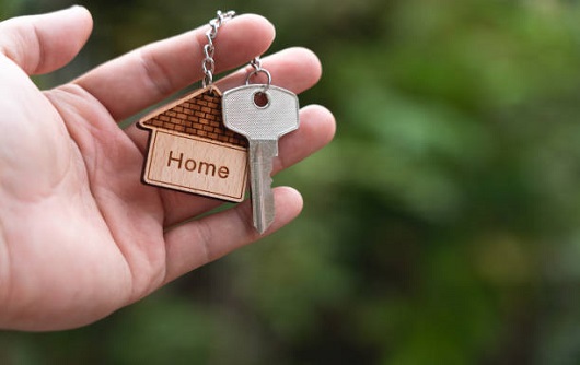 Home Key In Hand With House Keyring On Blur Green Garden Background, Copy Space